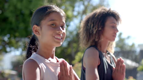 Happy-biracial-daughter-practicing-yoga-meditation-with-mother-sitting-in-sunny-garden,-slow-motion