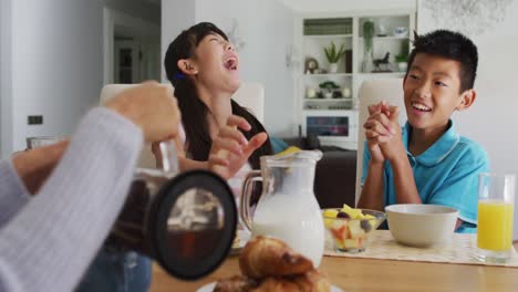 Glücklicher-Asiatischer-Bruder-Und-Schwester-In-Der-Küche,-Die-Frühstücken-Und-Mit-Den-Eltern-Lachen