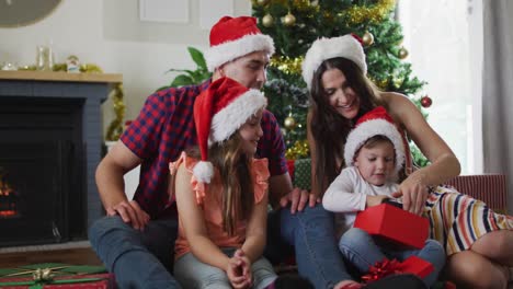 familia caucásica feliz con sombreros de santa desempaquetando regalos