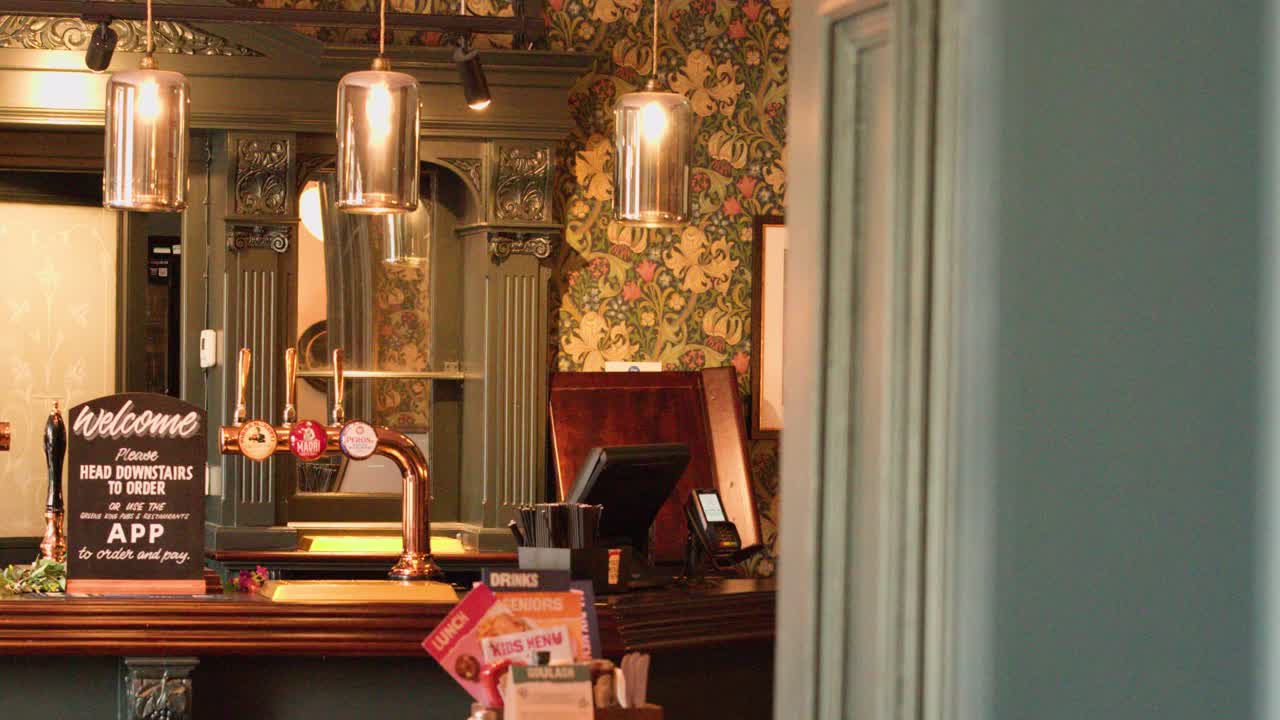 Camera glides past doorway, revealing warmly lit vintage pub with ornate decor and beer taps