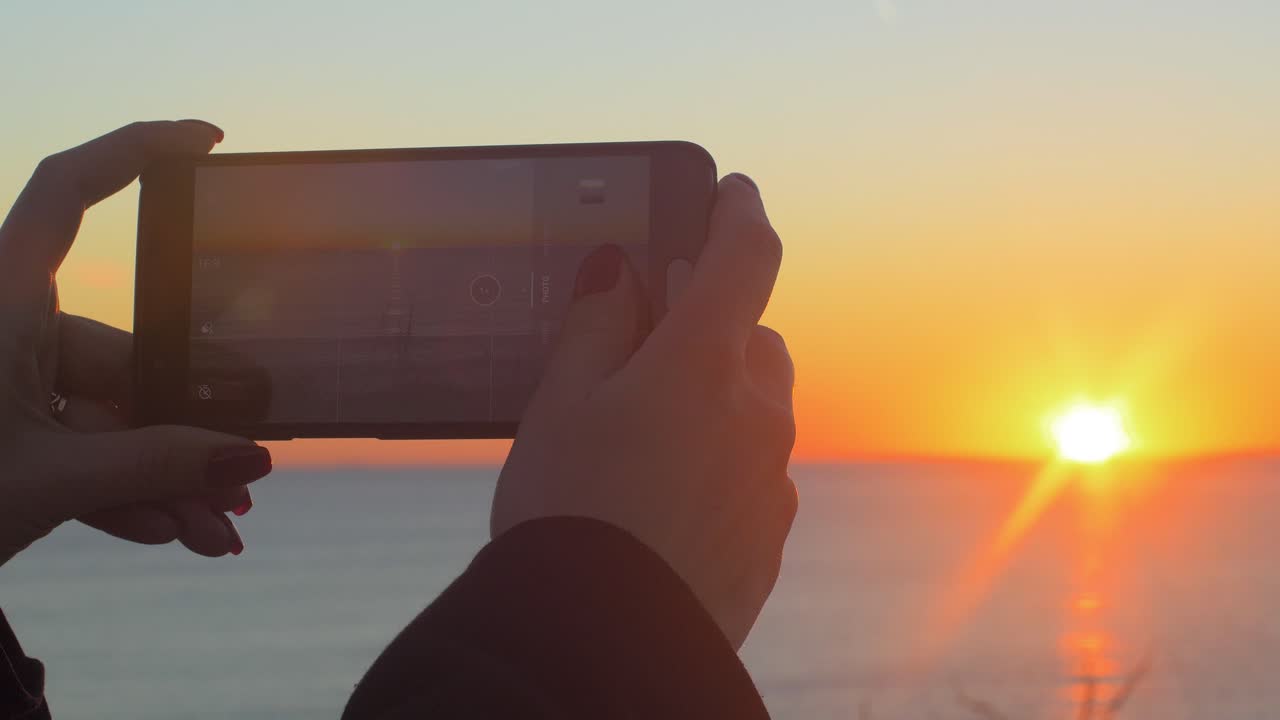 las chicas toman una foto de la puesta de sol con un teléfono inteligente