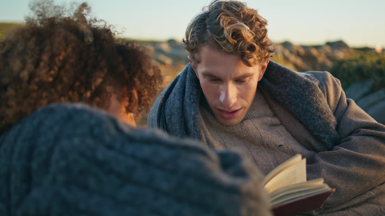 Handsome boyfriend reading literature at picnic for relaxed girlfriend closeup