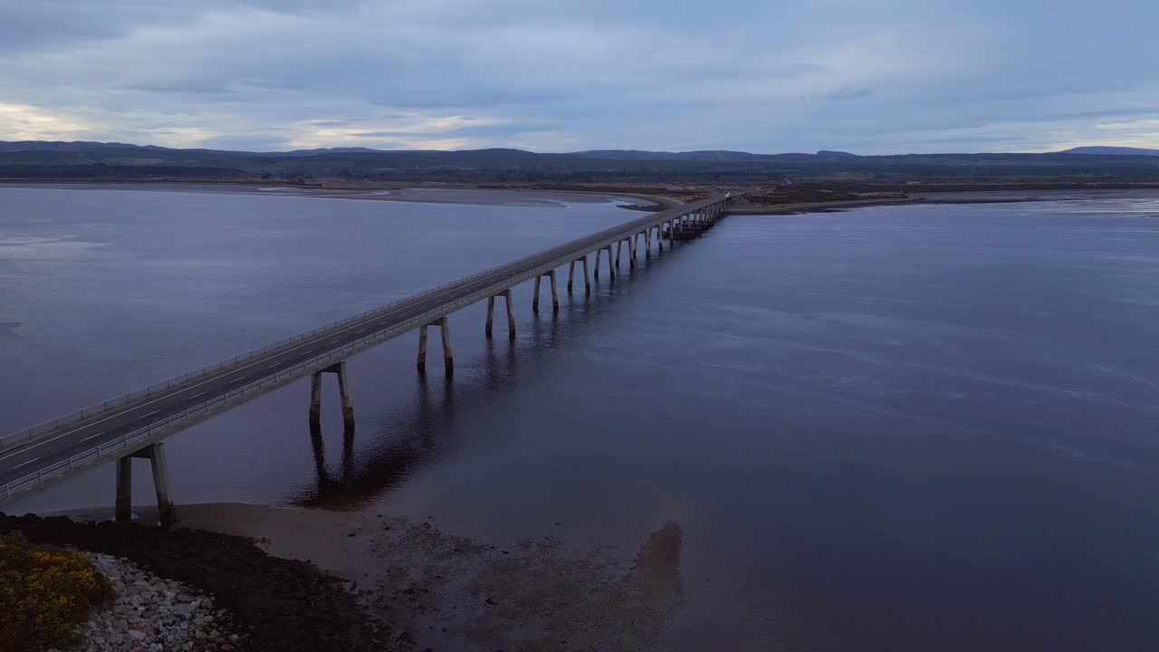 el dron se desliza con gracia hacia el puente de dornoch firth durante la encantadora hora azul del atardecer, revelando una vista impresionante del puente que se extiende sobre el brillante océano