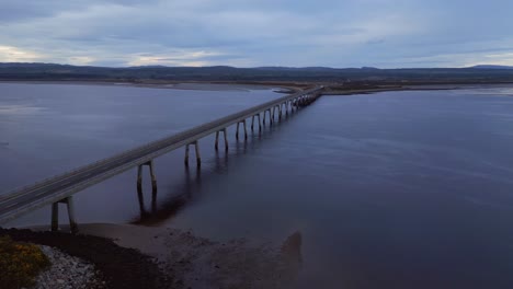 drone glides gracefully towards the dornoch firth bridge during the enchanting sunset blue hour, revealing a breathtaking view of the bridge spanning over the glistening ocean