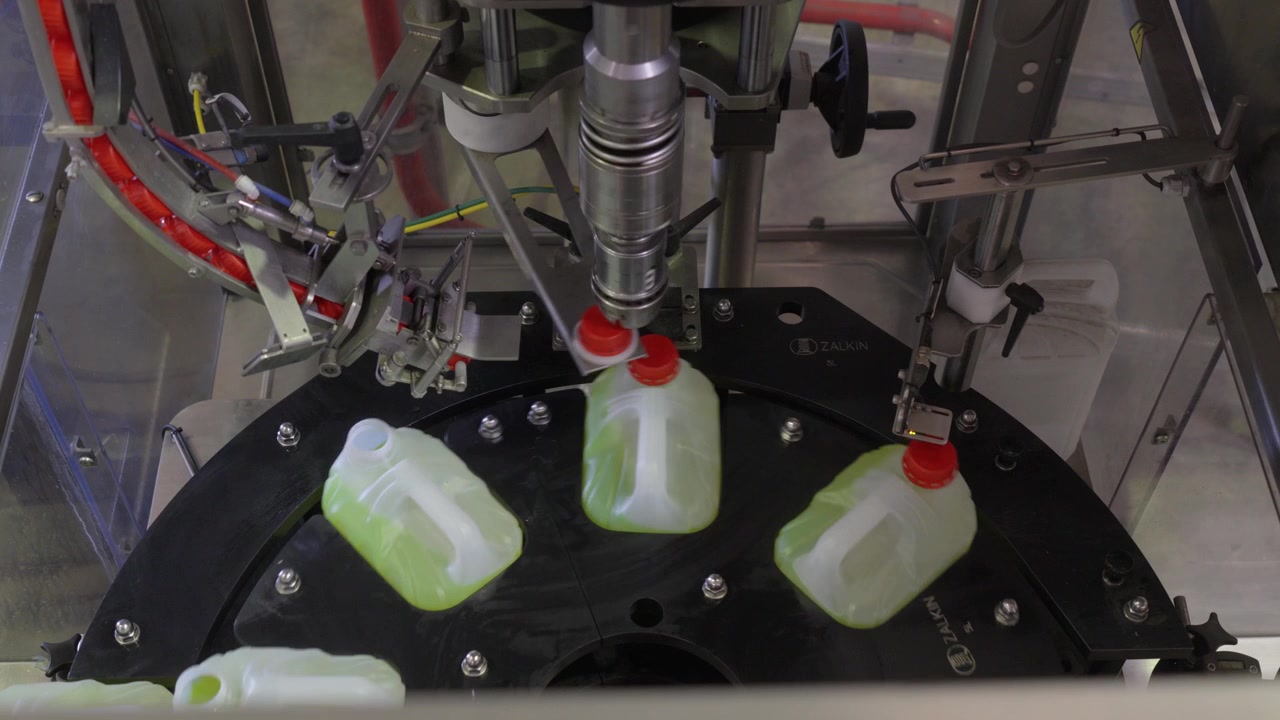 Static shot shows automated coolant fluid bottling and cap placement on a factory rotary line, efficient industrial mood.