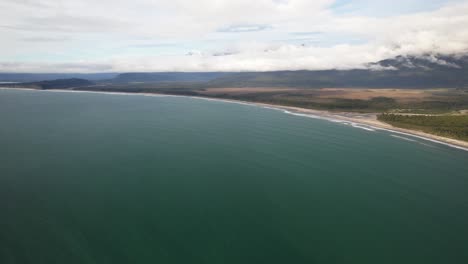 calm blue water of bruce bay with maori beach and mountains in the background in west coast, south island, new zealand. - aerial shot