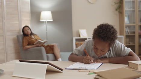 niño haciendo la tarea con la madre en el fondo