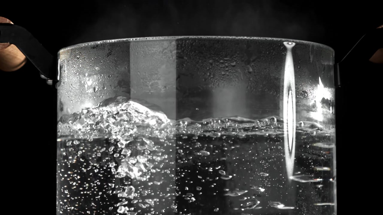 Acqua bollente che ribolle e produce vapore in una pentola trasparente