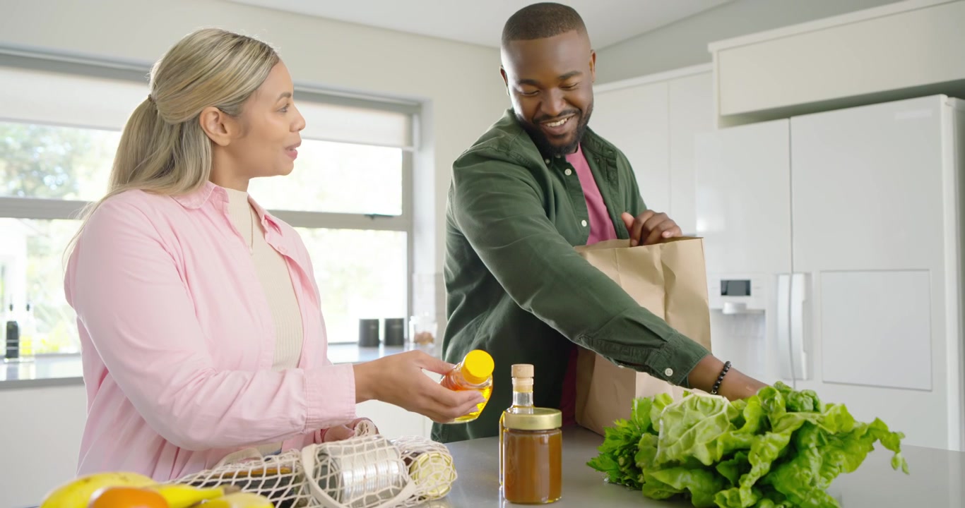 Casal desempacotando sacola de compras de papel pardo na ilha da cozinha depois das compras, lendo os rótulos