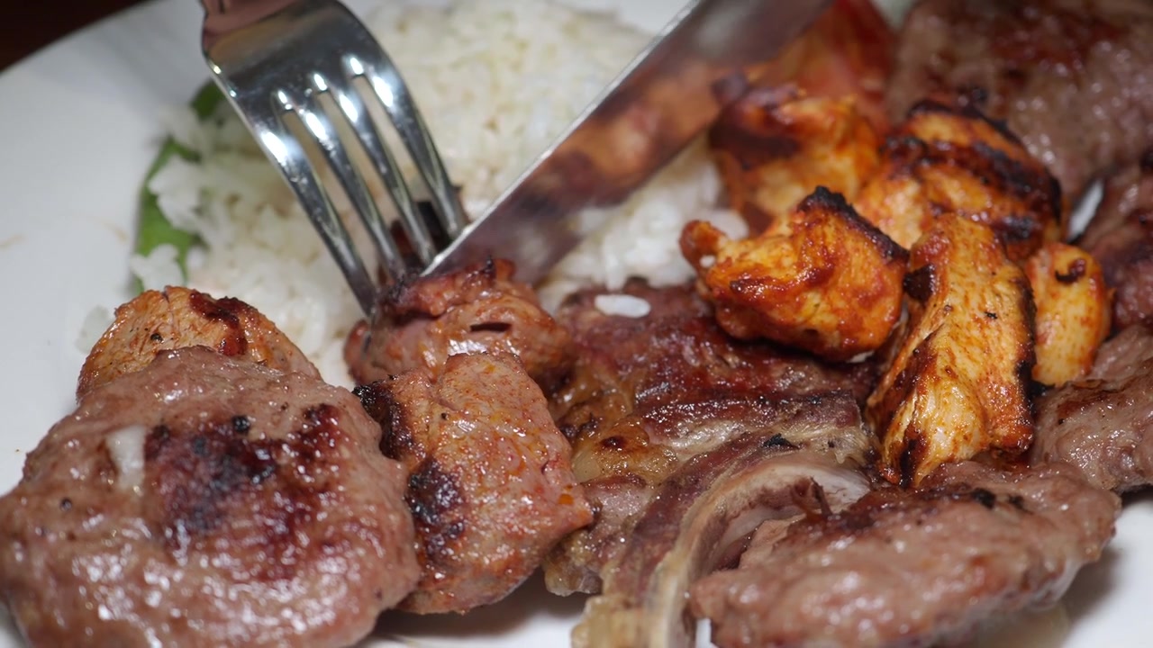 Cortando um Pedaço de Carne Grelhada de um Prato de Kebab Misto