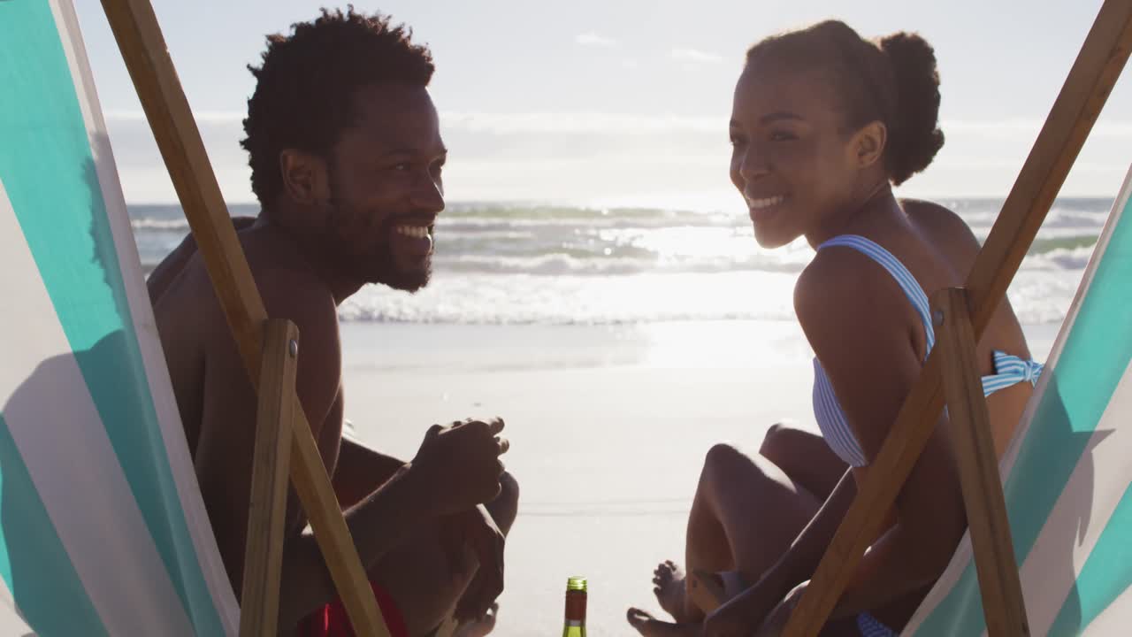 Portrait of african american couple smiling and sitting in deckchairs on the beach