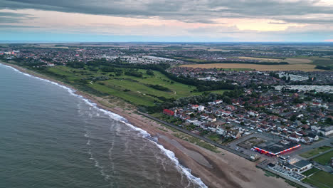 Enjoy-aerial-drone-shots-of-Skegness-town-by-the-sea-at-sunset,-showcasing-holiday-park,-beach,-and-caravans