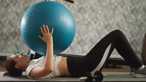 woman does abs training with fit-ball at home. athletic lady does crunches holding large ball on floor of domestic gym. sportswoman sits up lifting ball