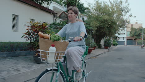 girl riding a bike with groceries, saying hi to someone