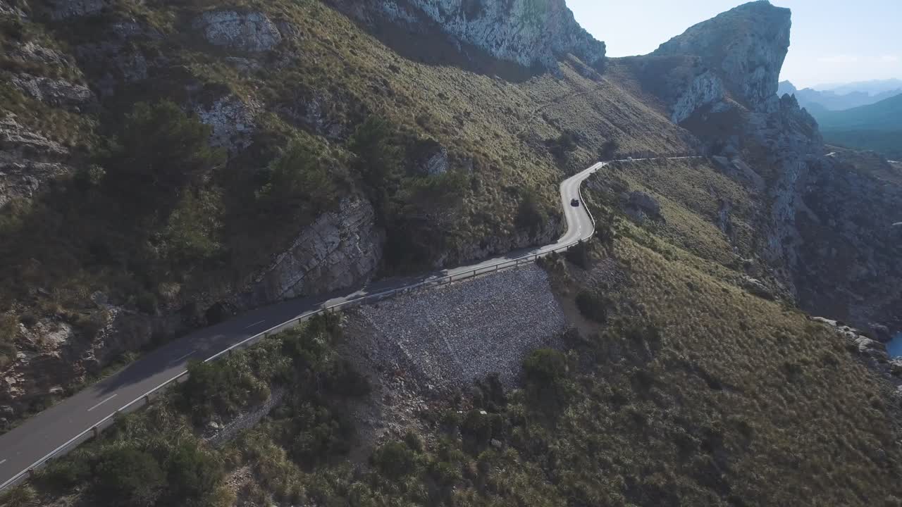 Breathtaking aerial footage in 4k of a car driving through the mountains on a small serpentine road next to a cliff in Mallorca, Spain