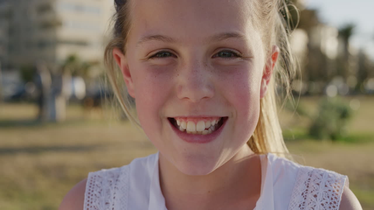 retrato de cerca hermosa niña pequeña riendo alegre disfrutando relajado día de vacaciones de verano en el cálido atardecer parque urbano viento soplando el cabello