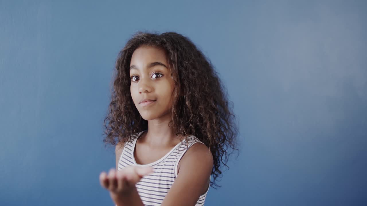 Happy african american girl using sign language on blue background, slow motion