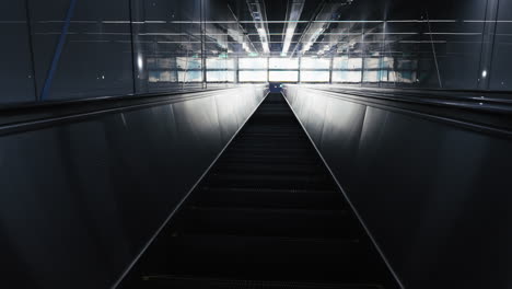 modern dark escalator leading towards bright reflective surfaces