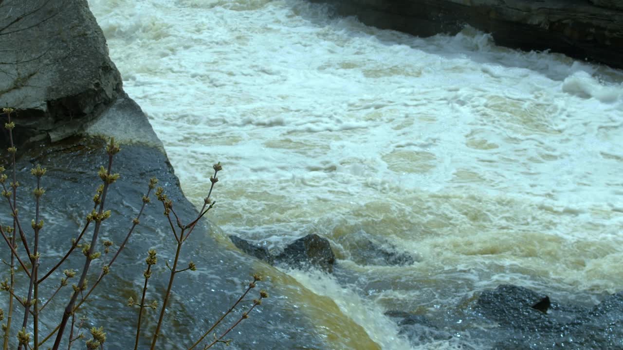Water from a swollen river pours over a rocky cliff in slow motion