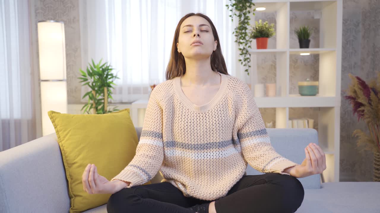 mujer joven sentada en el sofá en casa meditando con los ojos cerrados.