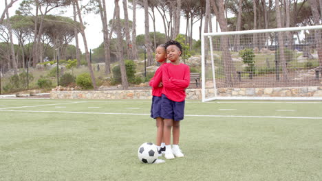 multiracial boys standing on soccer field smiling with soccer ball