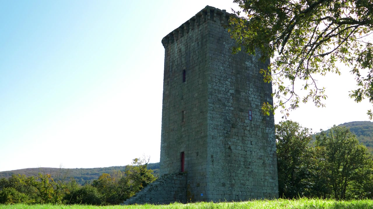 Tower of A Forxa rises beside leafy trees and green grass in Porqueira, Ourense, Galicia