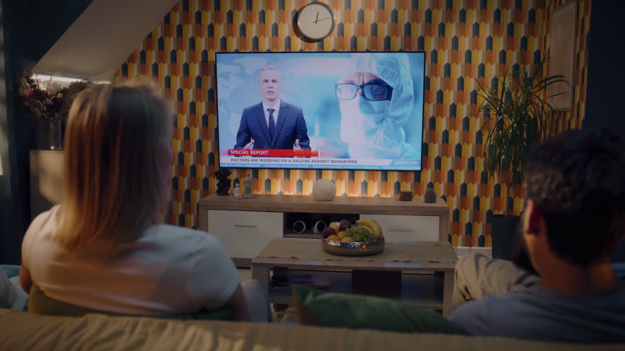 부부가 원이 천연두 백신에 대한 뉴스 보도를 보고 있습니다.