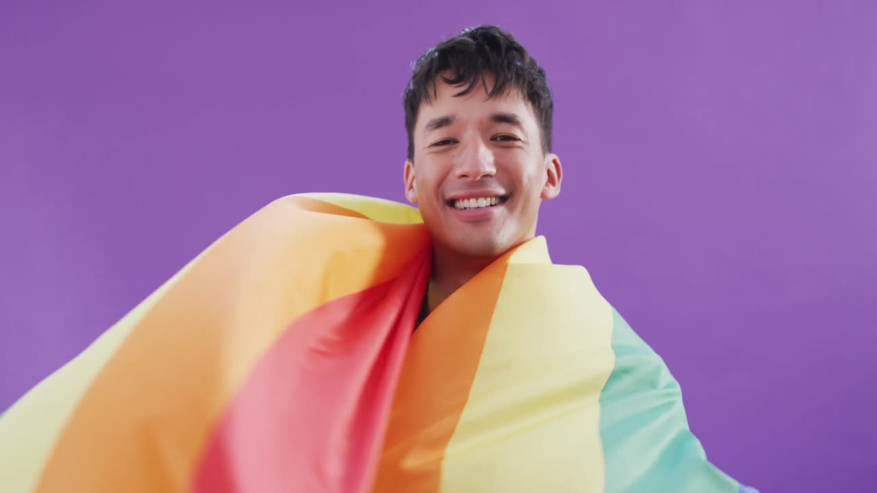 retrato de un feliz hombre biracial sosteniendo una bandera lgbt con los brazos abiertos