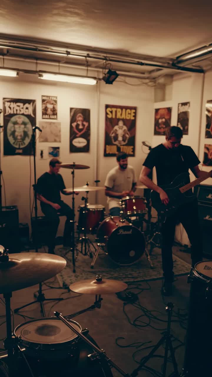 A band rehearses in a dimly lit room, captured from a low angle. The video style emphasizes a raw
