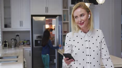 Woman-wearing-earphones-talking-on-smartphone-in-the-kitchen