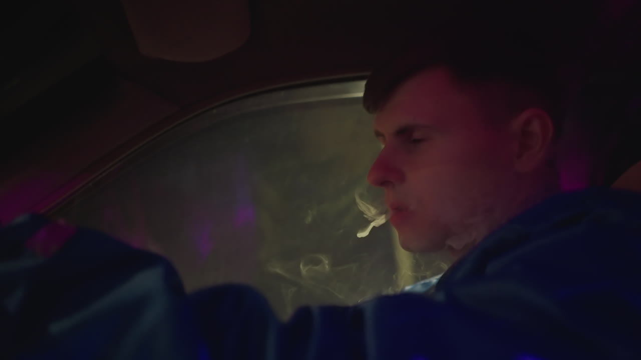night rain soaked driver exhaling vapor beside wet windshield. Intimate interior shots show man inhaling and releasing cloud, raindrops on glass, neon reflections, tense quiet, smoky atmosphere