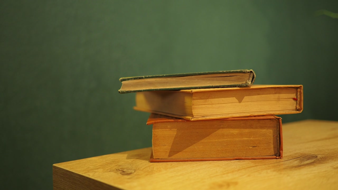 Hand Removing a Vintage Book from a Stack on a Wooden Table