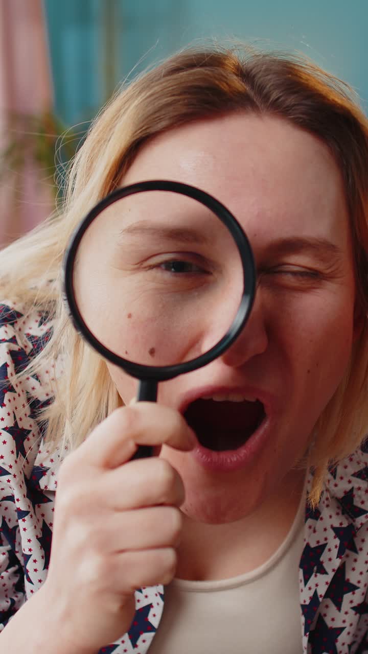 Woman holding magnifying glass near face looking into camera with big zoomed funny eye analyzing