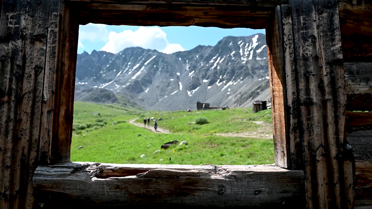 Terk edilmiş bir madenci kulübesinin penceresinden dağların görüntüsü
