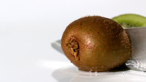 kiwi being sliced in half on wet white background