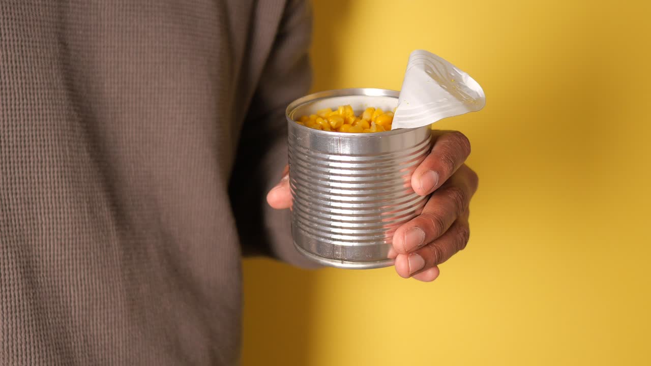 Hand Scooping Canned Corn from a Metal Can with a Spoon
