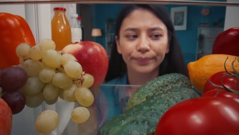woman looking into a fridge full of vegetables and fruits but appears disappointed