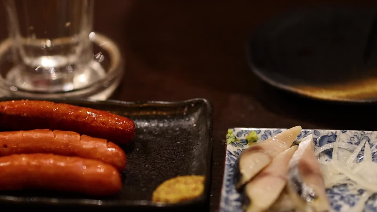 Close-up of sausages being served with chopsticks, accompanied by mustard and pickled vegetables.