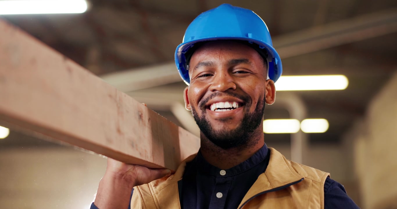 Smiling Construction Worker Carrying Wooden Plank in Workshop