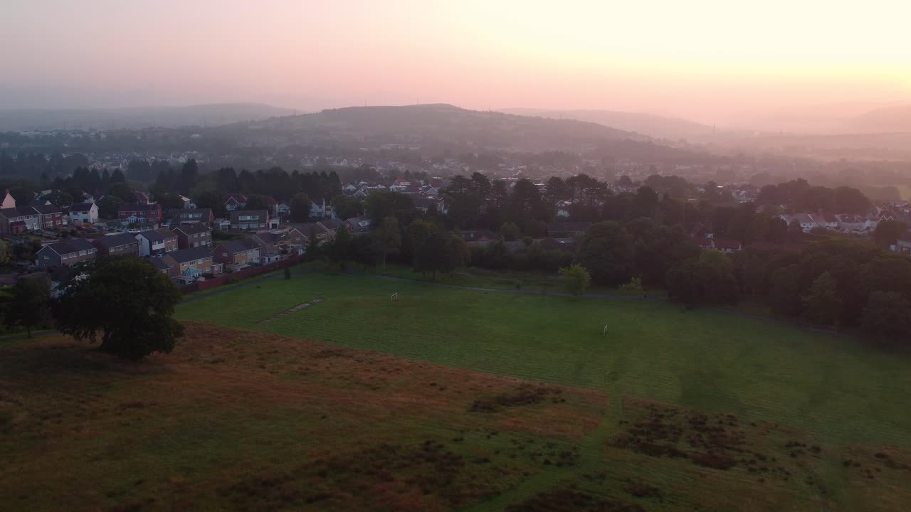 Beautiful Wide View of Recreational Park with Trees and Surrounding Housing with Silhouetted Dramatic Hills in Background with Sunrise Haze Filling Valley. Drone View of Densely Populated Streets