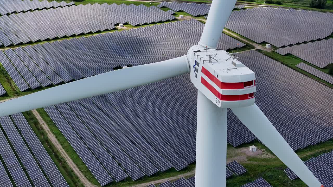 풍력 터빈은 태양 전지 중간에 서 있으며, 태양 전지판의 줄로 둘러싸여 있습니다.