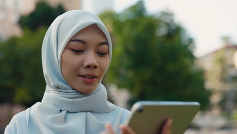 Young Muslim woman in hijab using a tablet outdoors