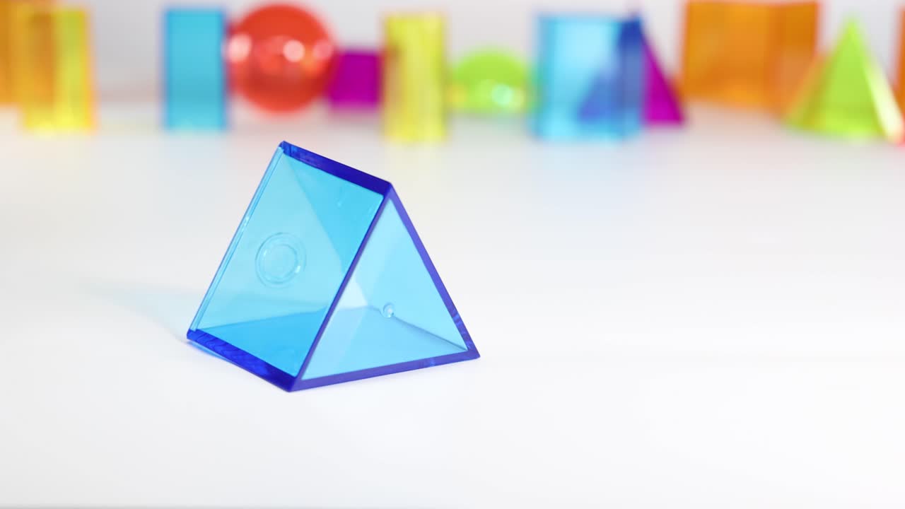 A hand interacts with colorful 3D geometric shapes on a white surface, demonstrating movement and balance