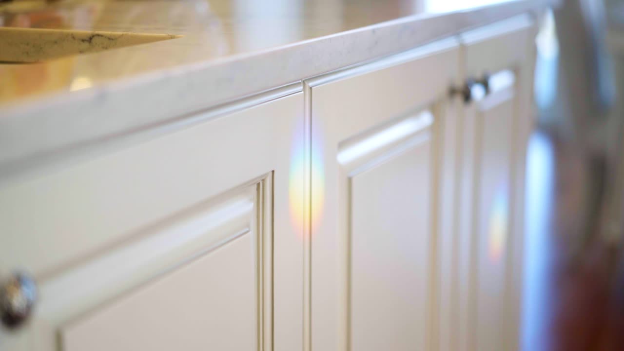 Elegant white cupboards with a white marble counter top with rainbow lights reflecting in a luxurious home
