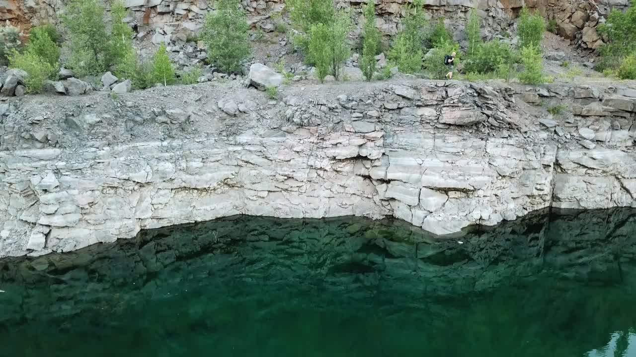 Clean water background near the stone slope and the tourist walking on it. Aerial filming of a rocky canyon with a wanderer outdoors. Motion bottom up