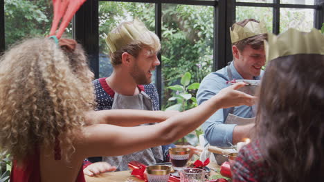 group of friends sitting around dining table at home enjoying christmas dinner together