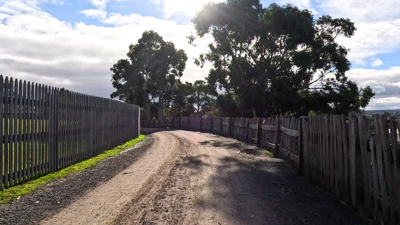 un camino de tierra con cercas de madera y árboles