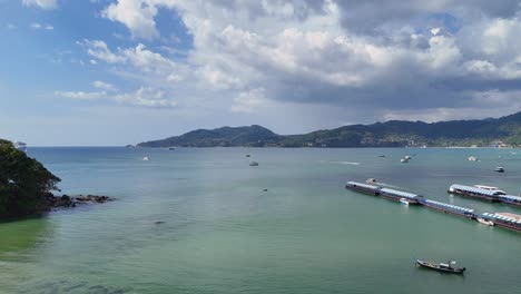 drone footage captures serene patong bay with longtail boats and a pier under partly cloudy skies, showcasing phuket's coastal beauty