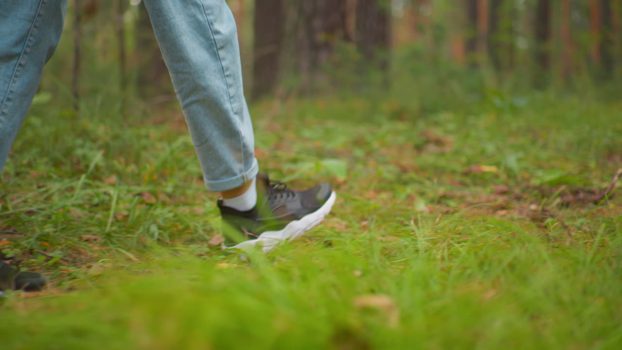 close-up of woman's feet walking on forest floor wearing black sneakers ...