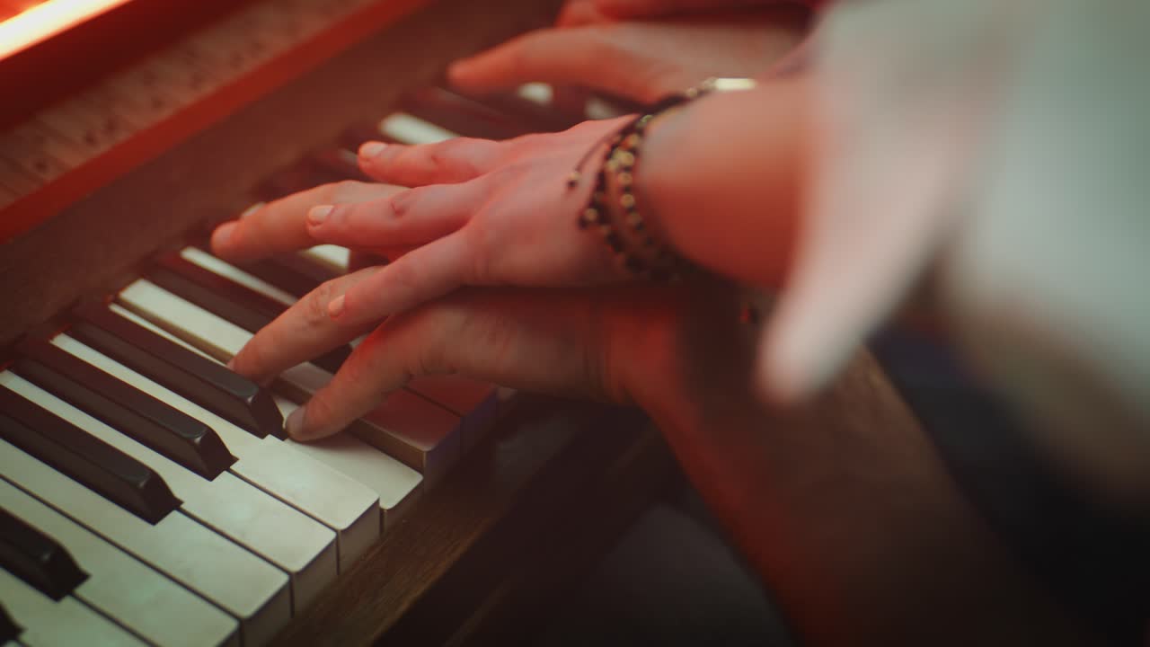 A cinematic top-down shot of a piano keyboard illuminated with a vibrant pink glow as fingers rest on the keys